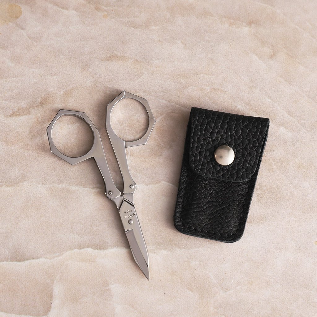 Nogent stainless steel foldable scissors fully extended beside a black leather case.