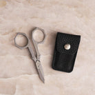 Nogent stainless steel foldable scissors fully extended beside a black leather case.