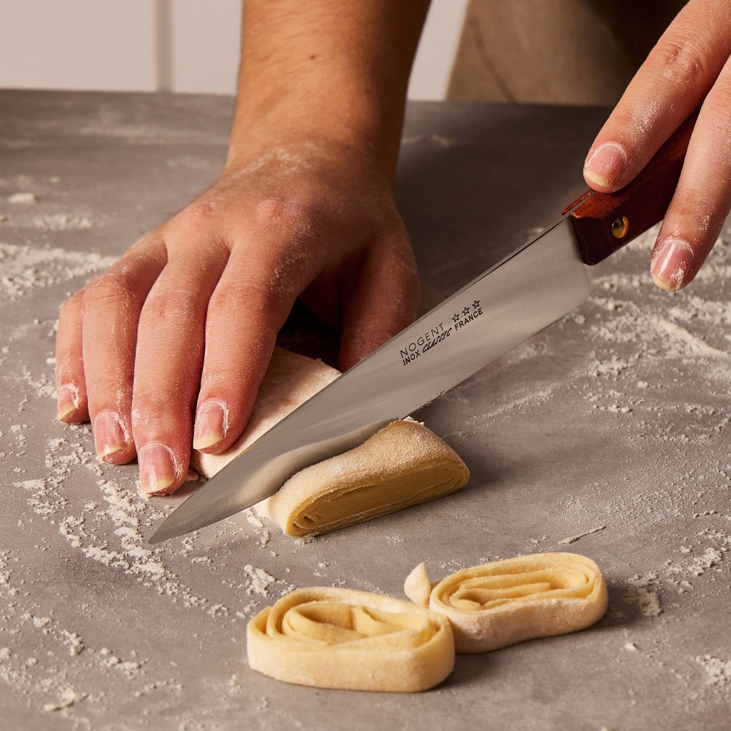 Hands holding knife and cutting raw pasta.