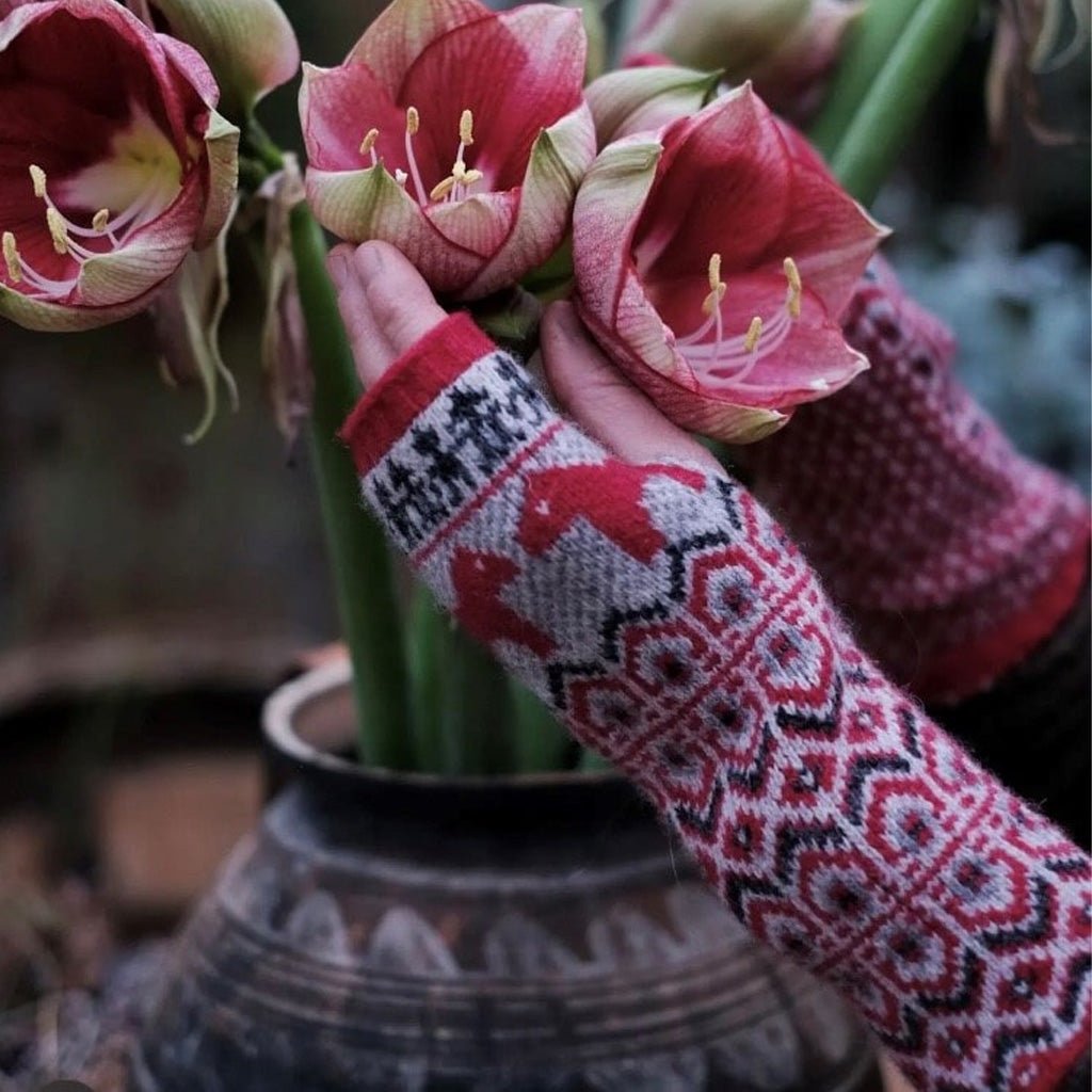 Hands wearing red wool wrist warmers arranging flowers.