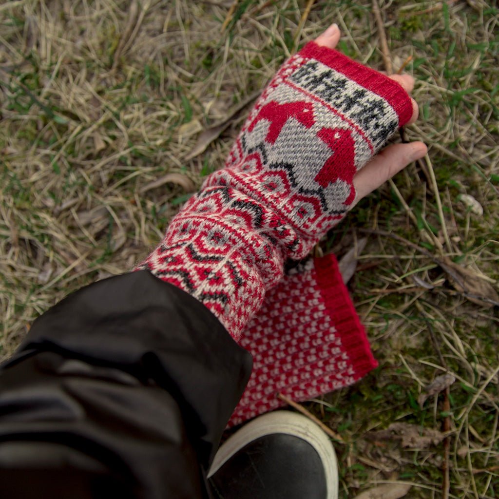 Hand wearing red wool wrist warmer with black jacket.