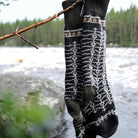 Pair of patterned wool socks hanging on tree branch in front of water setting.