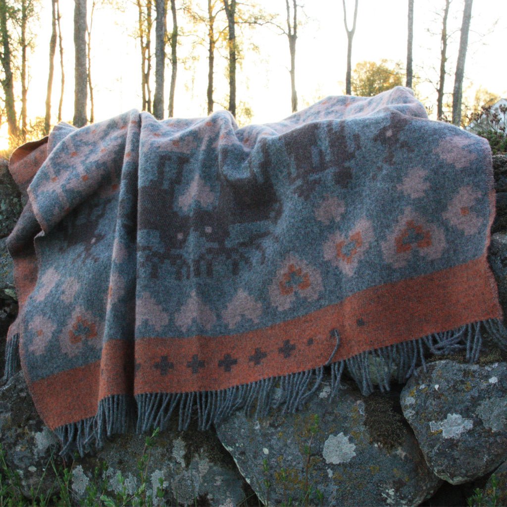 Wool blanket with Nordic pattern laid out over mossy rocks.