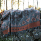 Wool blanket with Nordic pattern laid out over mossy rocks.