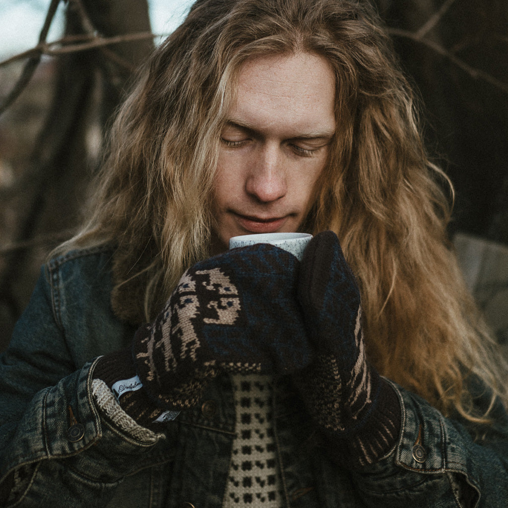 Model wearing wool mittens and holding mug.