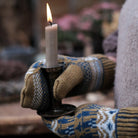 Person wearing patterned wool mittens and carrying lit candlestick.