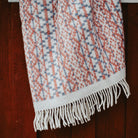Lycksele wool blanket with white fringe in front of wood wall.