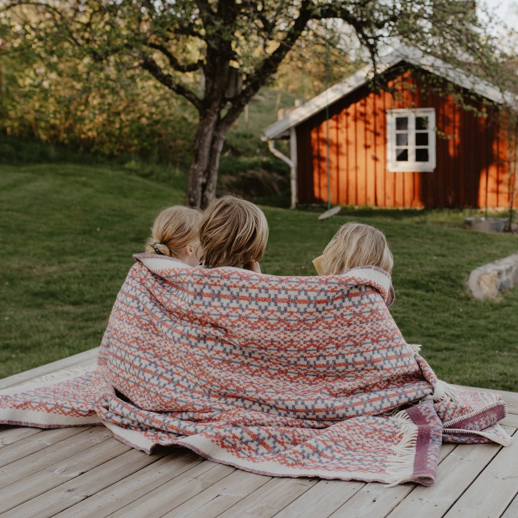 Three children wrapped in Lycksele wool blanket in backyard.