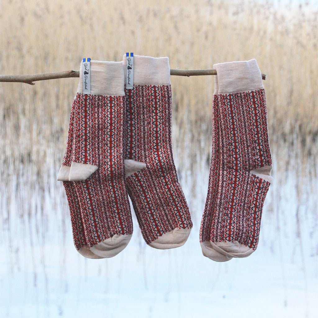 Three pairs of patterned wool socks hanging on branch in natural setting.