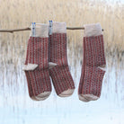 Three pairs of patterned wool socks hanging on branch in natural setting.