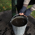 Hands wearing wool wrist warmers, carrying metal bucket of water.