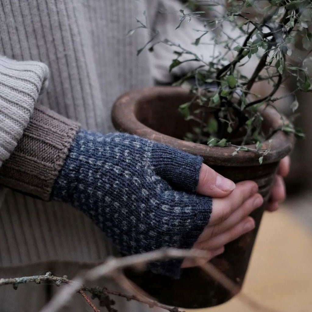 Hand wearing wool wrist warmer, holding potted plant.