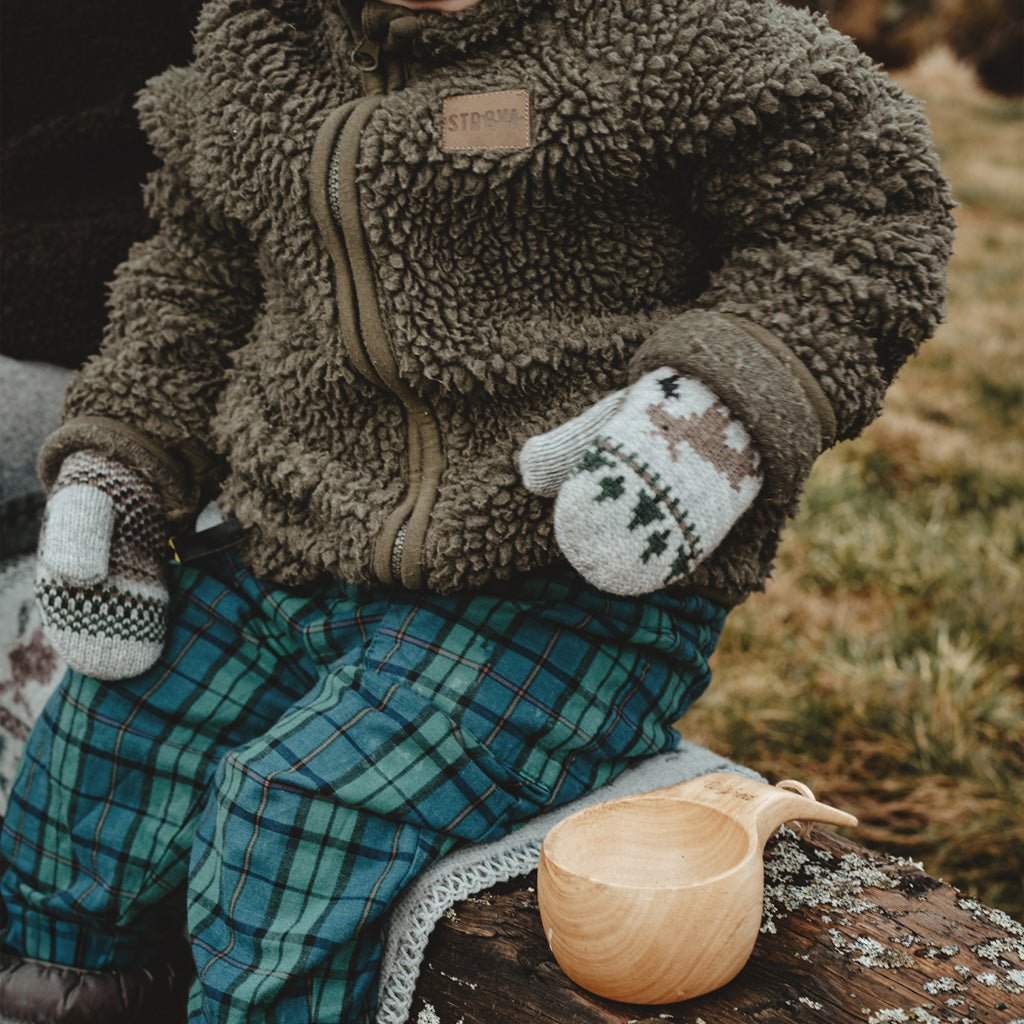 Child wearing gray wool mittens in outdoor setting.