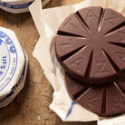 Round chocolate tablets with 'TAZA' branding on a wooden surface.