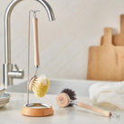 A wooden dish brush with light bristles hanging on hook on kitchen counter next to sink