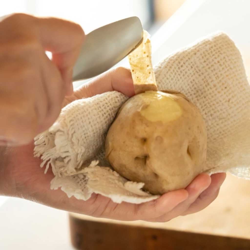 Person peeling a potato in a cloth, using a tong as a scraper.
