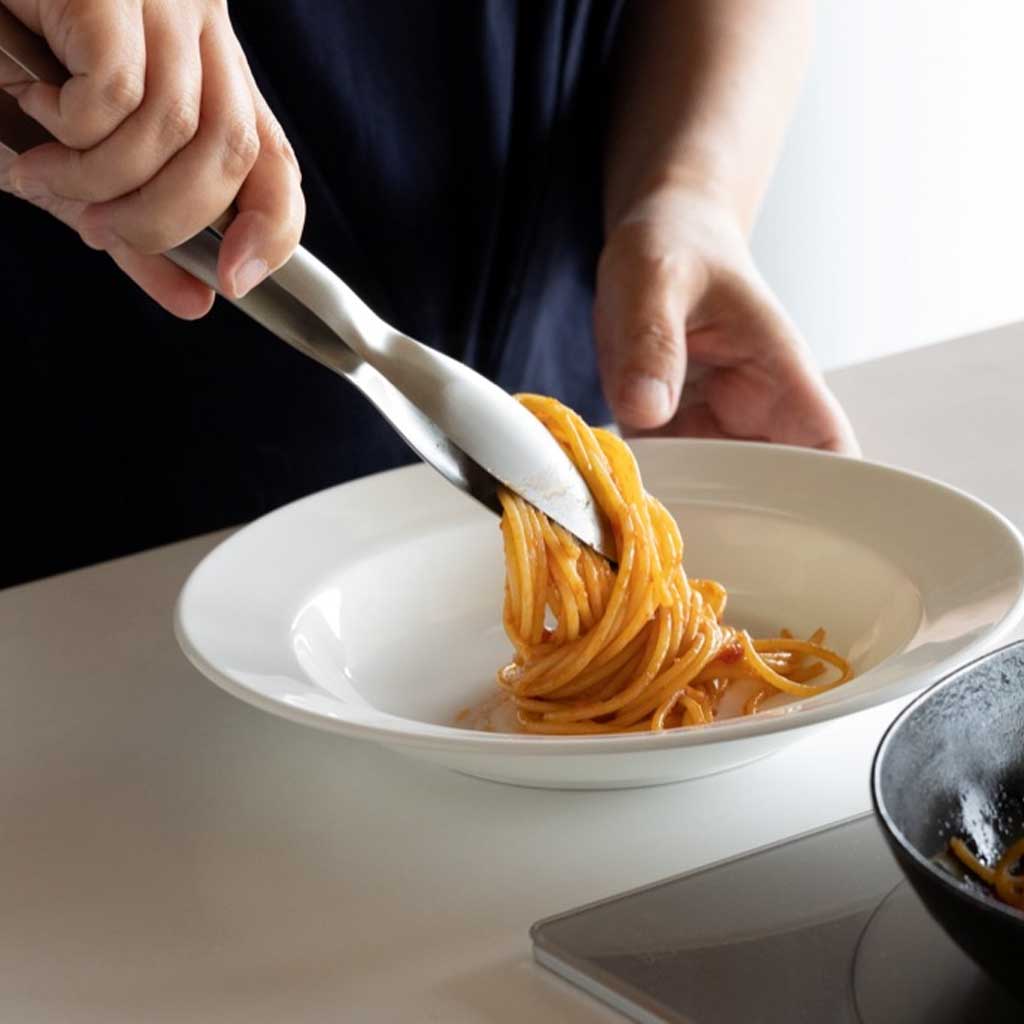 Person using a pair of tongs to serve spaghetti onto a white plate.