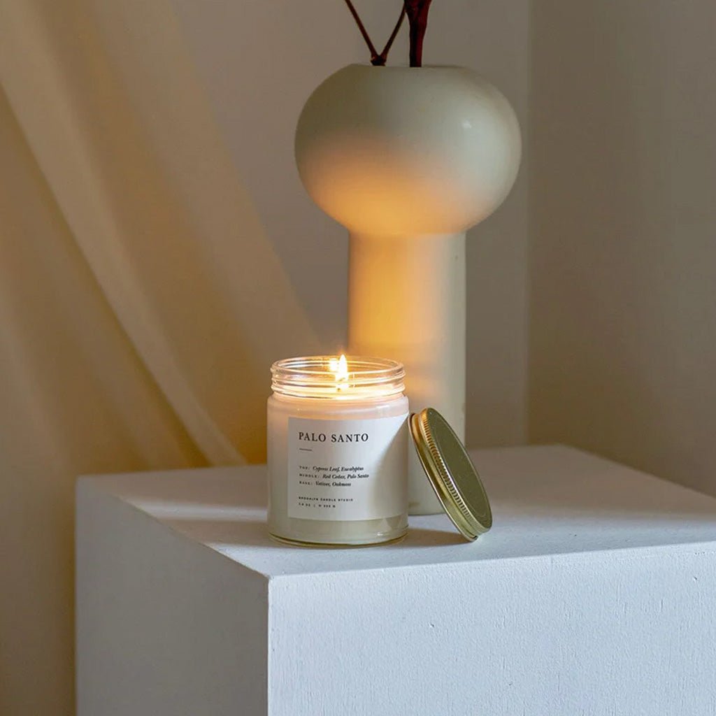 Candle labeled 'Palo Santo' on a white surface with a softly lit background