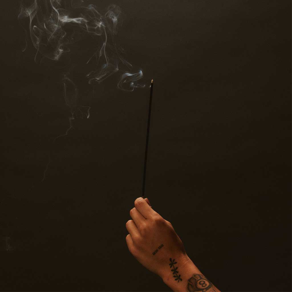 Hand holding an incense stick with smoke against a dark background