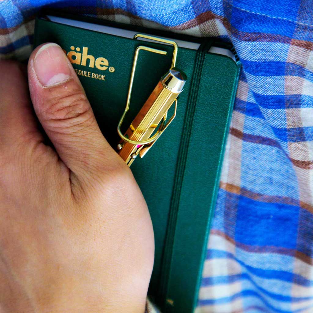 Pen on pen clip on green notebook being held against plaid fabric