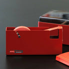 Large red steel tape dispenser on a dark surface with a gray background