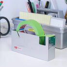 Metallic tape holder with green tape on a desk with office supplies.