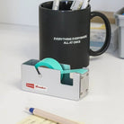 Black mug with text, tape dispenser, and pencil on a desk