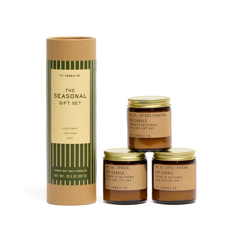 Three P.F. Candle Co. mini candles in amber jars with kraft labels and gold lids next to kraft tube packaging with festive green label on white background