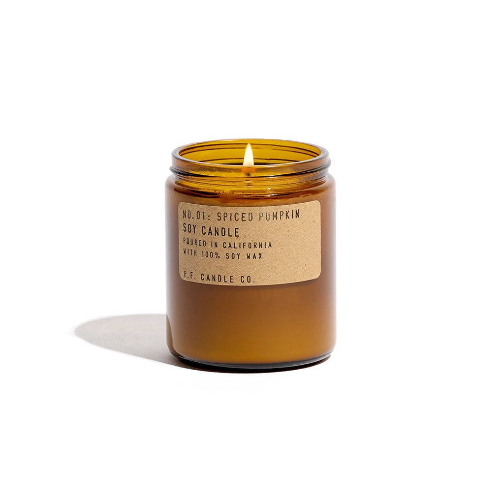 A spiced pumpkin candle burns inside an amber glass jar with the lid off. 