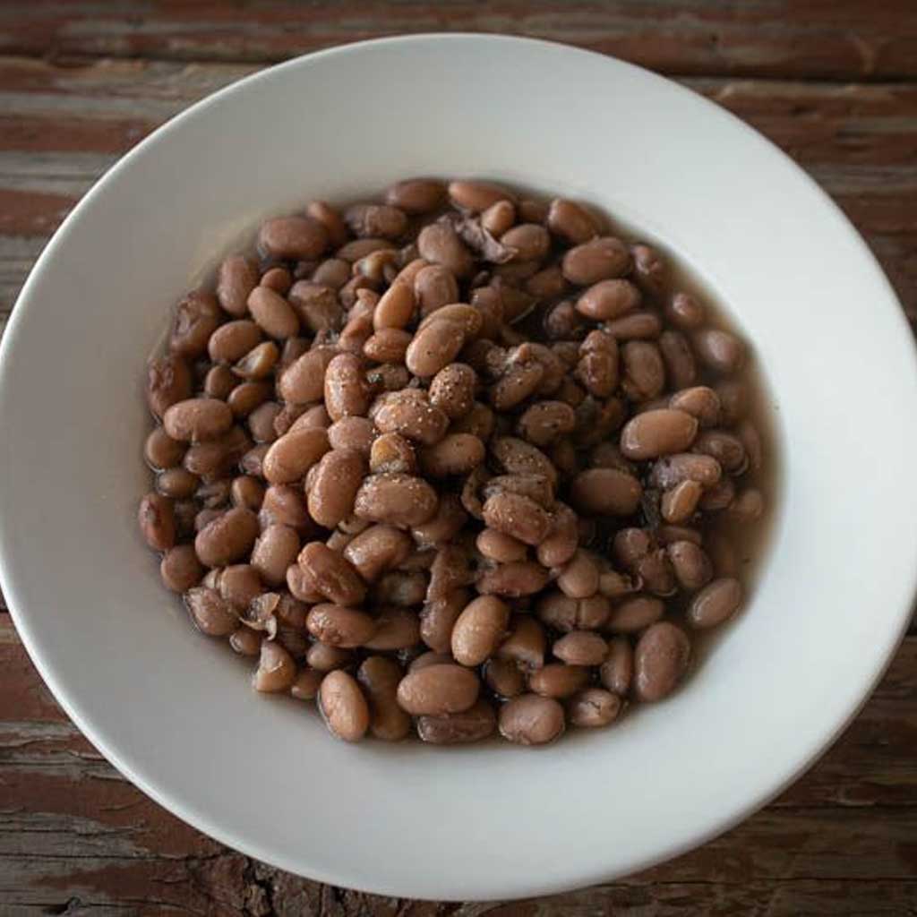 White bowl filled with pinto beans on a wooden surface