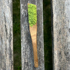 Wooden spoon with powdered sencha green tea against natural surface