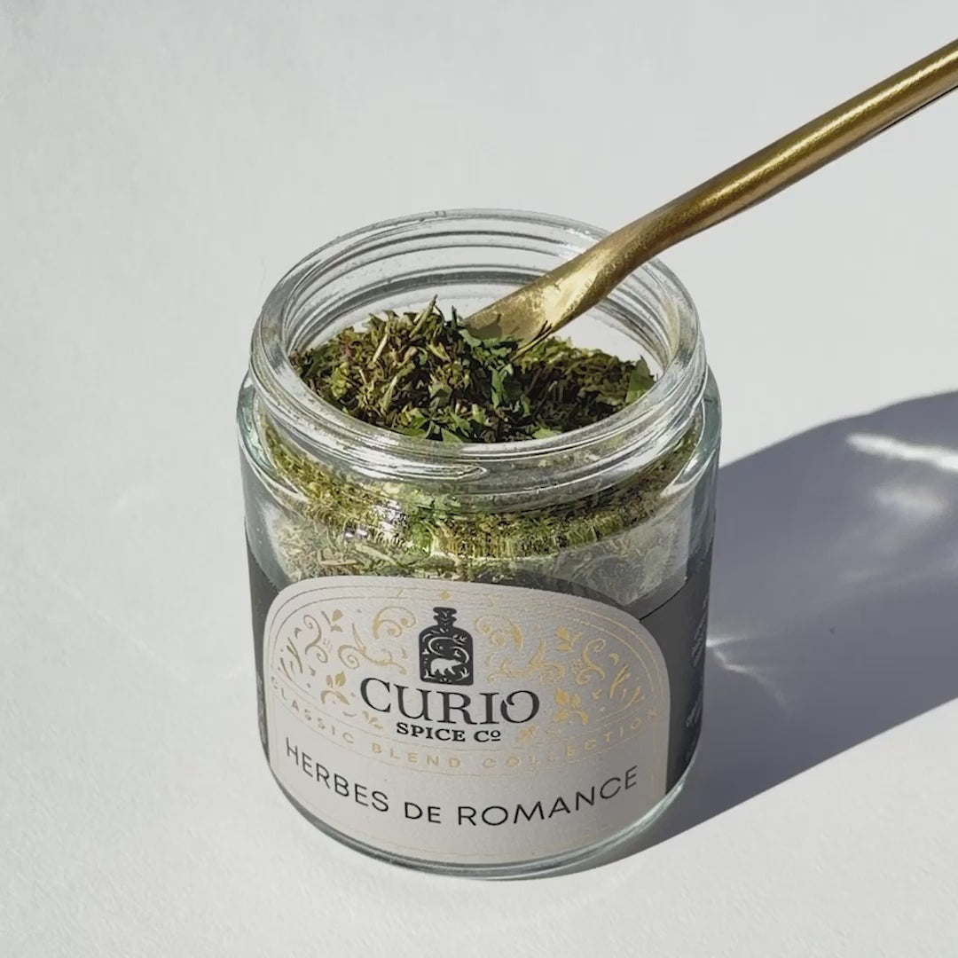 Video of spoon dipping into jar of Herbes de Romance blend on white background