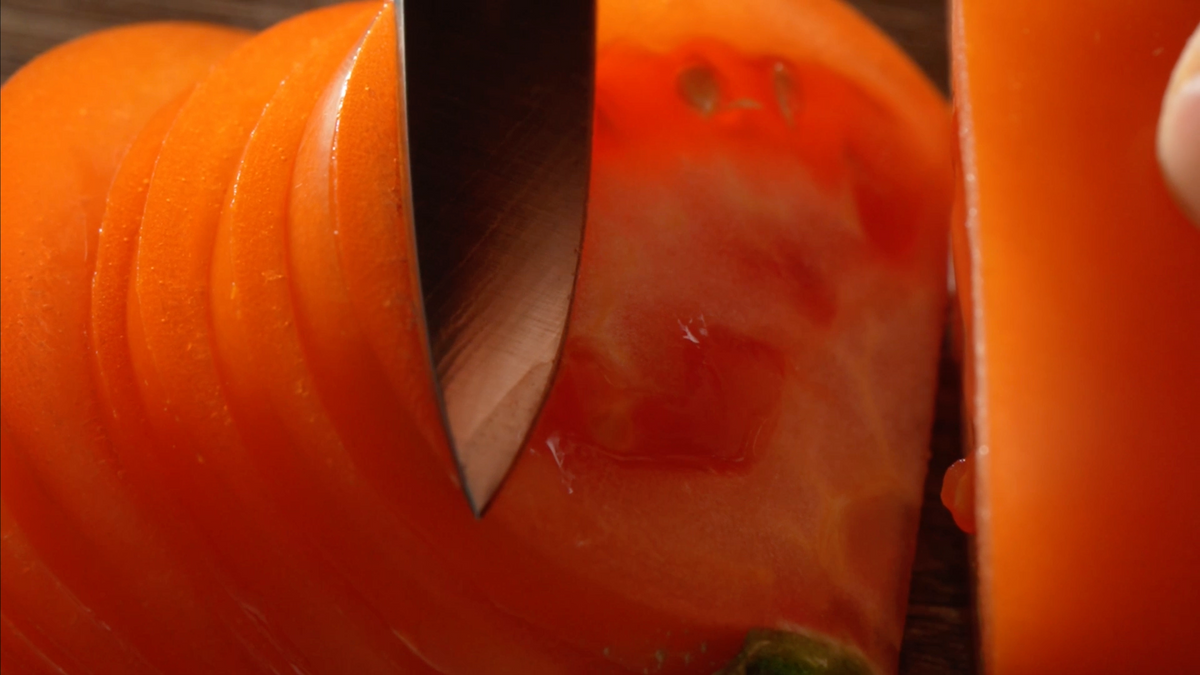 Video of Nogent tomato and utility knife slicing produce on wooden surface.