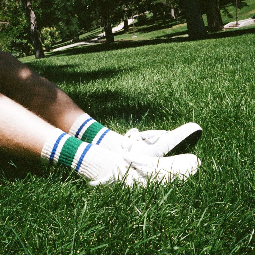 Close-up of a person wearing white socks with green and blue stripes on grass