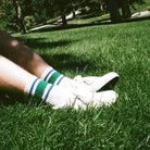 Close-up of a person wearing white socks with green and blue stripes on grass