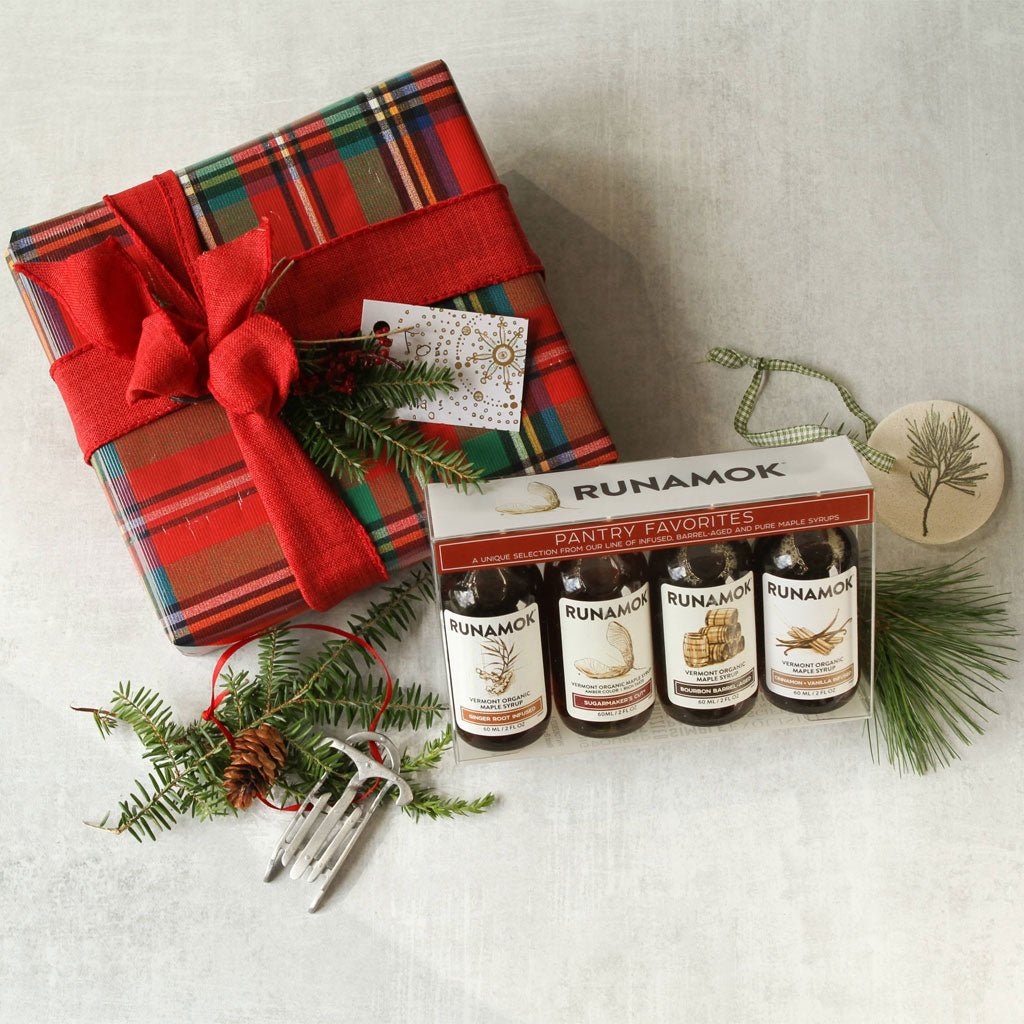 Set of Runamok maple syrup bottles next to festive wrapped present and sprigs of holly.