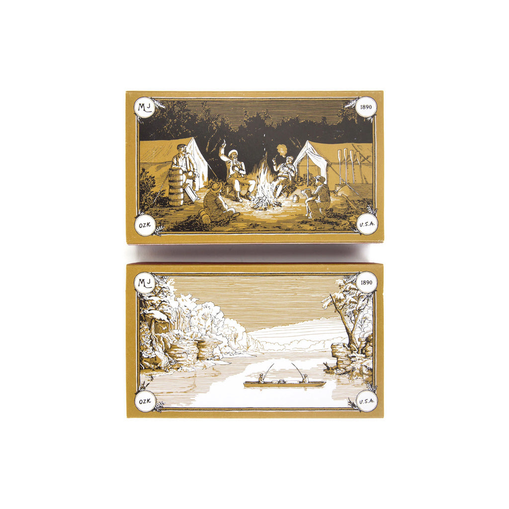 Two rectangular match boxes stacked vertically on a white background. The top box features a sepia-toned illustration of figures around a campfire with tents, and the bottom box features a sepia-toned landscape with trees and a boat.