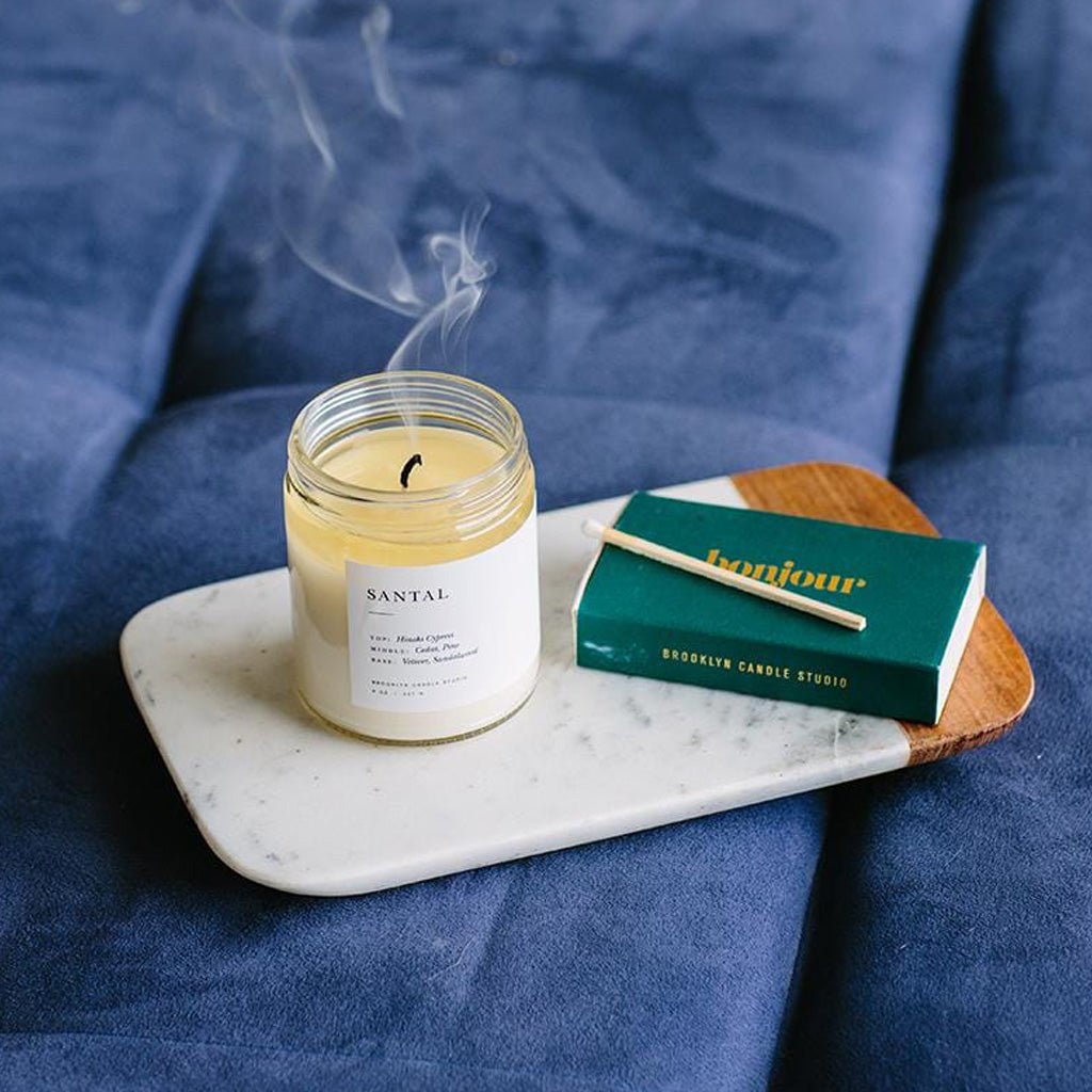 Scented Santal candle with a matchbox on a marble tray against a blue fabric background