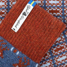 Close-up of a knitted textile product showing a rust-orange ribbed section with a white fabric label reading 'Ojbro Vantfabrik' and a blue-and-orange patterned knit section.