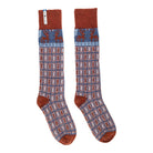 A pair of patterned knit socks with a rust brown cuff, heel, and toe, featuring a blue upper band with red reindeer motifs and a red, blue, and white geometric pattern below.