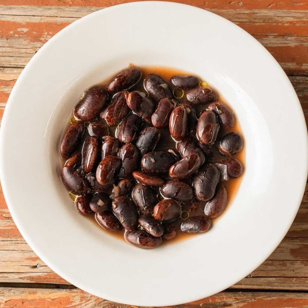 White bowl filled with dark red scarlet runner beans on a wooden surface