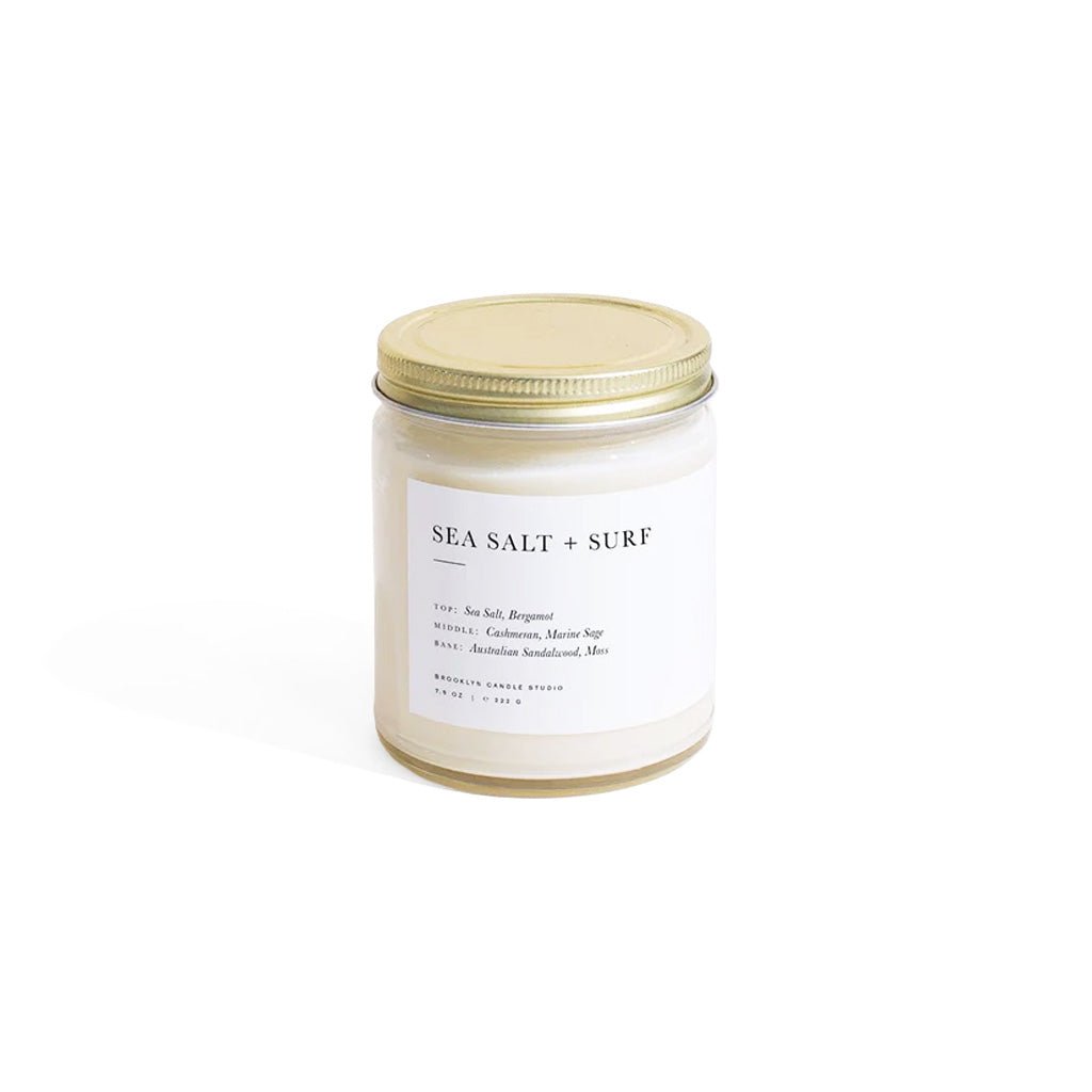 Candle jar labeled 'Sea Salt + Surf' with a gold lid on a white background