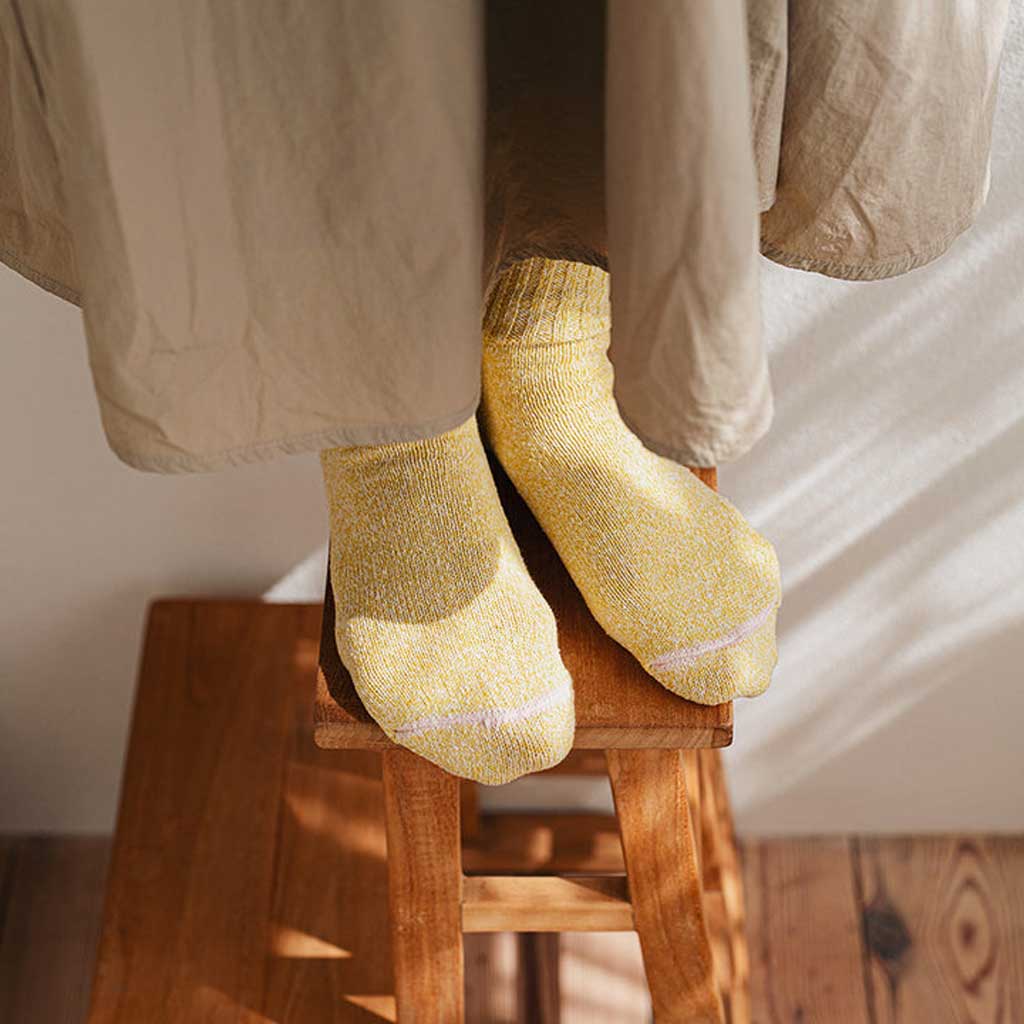 Person wearing yellow socks sitting on a wooden stool with a neutral background
