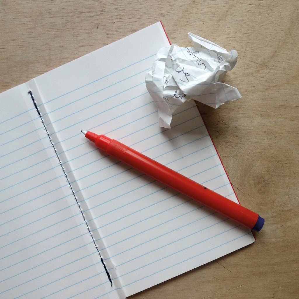 Lined notebook with crumpled piece of paper and red pen on wooden background