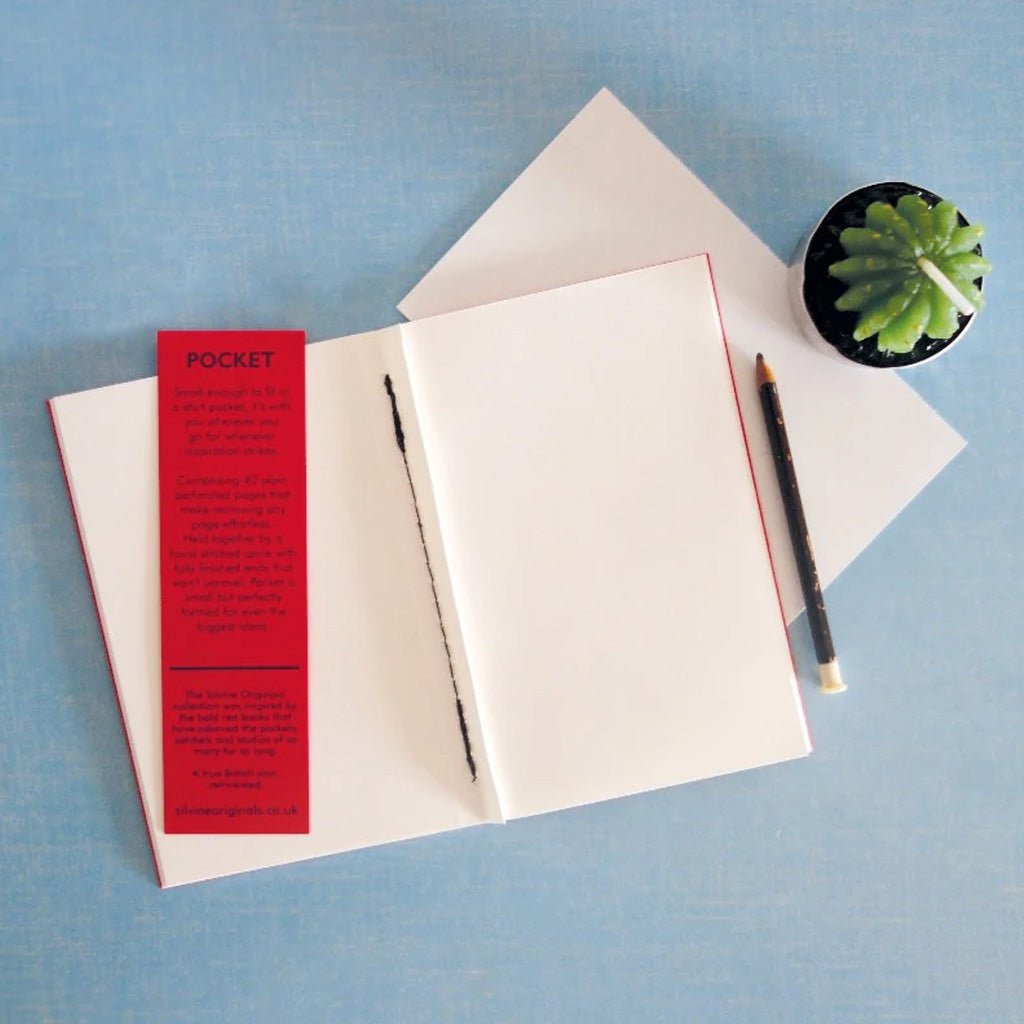 Open blank pocket notebook next to pencil and plant on blue background