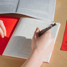 Hand holding pencil writing in red exercise notebook with lined pages on wooden background
