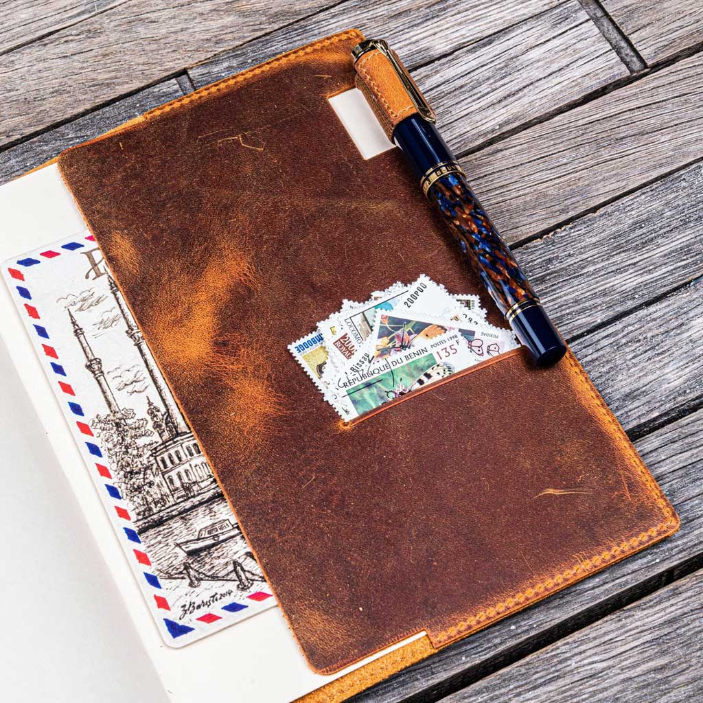 Brown leather notebook with a pen and stamps on a wooden surface