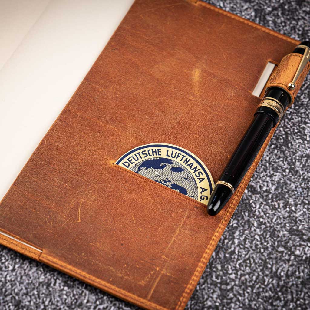 Brown leather notebook with Lufthansa logo and a pen on a textured surface