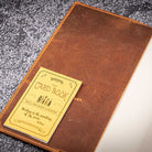 Brown leather notebook cover with gold card on a textured surface