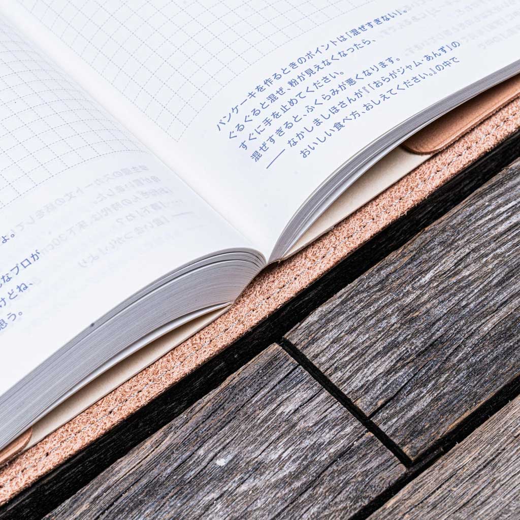 Open book with Japanese text in natural undyed leather notebook cover on a wooden surface